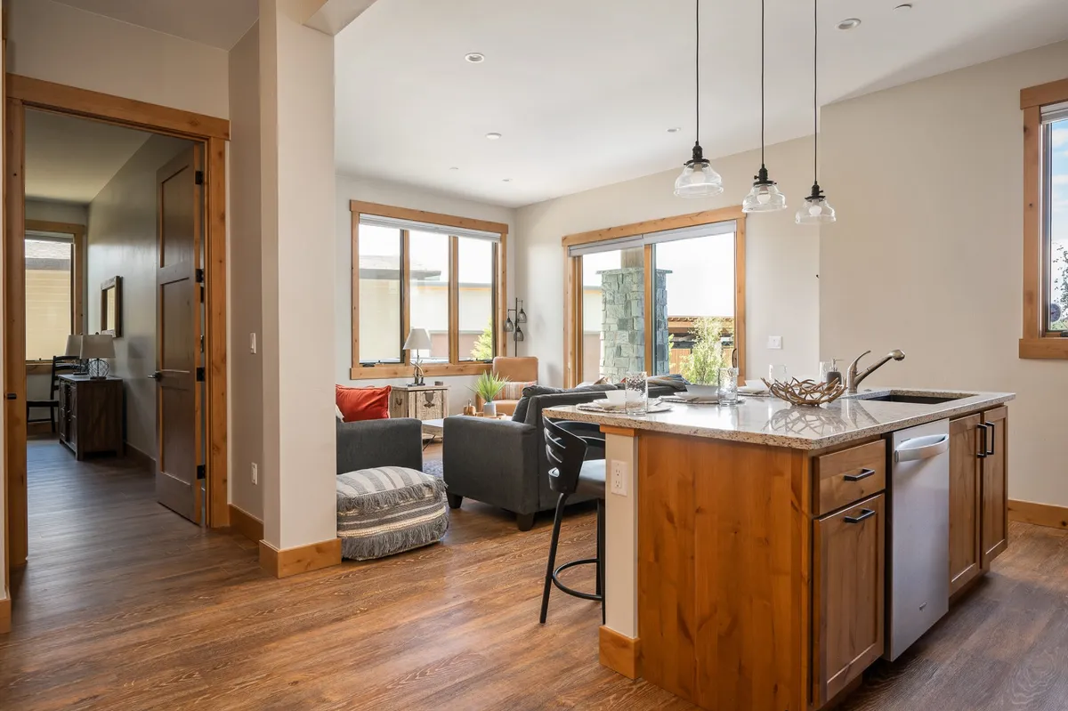 A broad view of the open-plan living area, with a kitchen island seamlessly transitioning into a spacious seating area. Large windows flood the space with natural light and provide panoramic views of the surrounding landscape, enhancing the open, communal atmosphere.