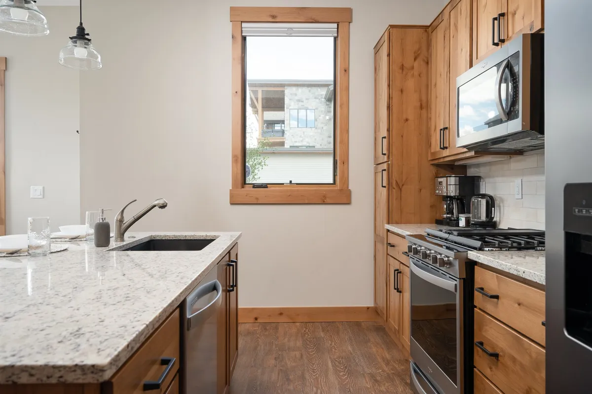 This image features a granite countertop, stainless steel appliances, warm wood cabinets, and a window view. The kitchen is well-organized, modern, and inviting, with ample space for cooking and socializing.