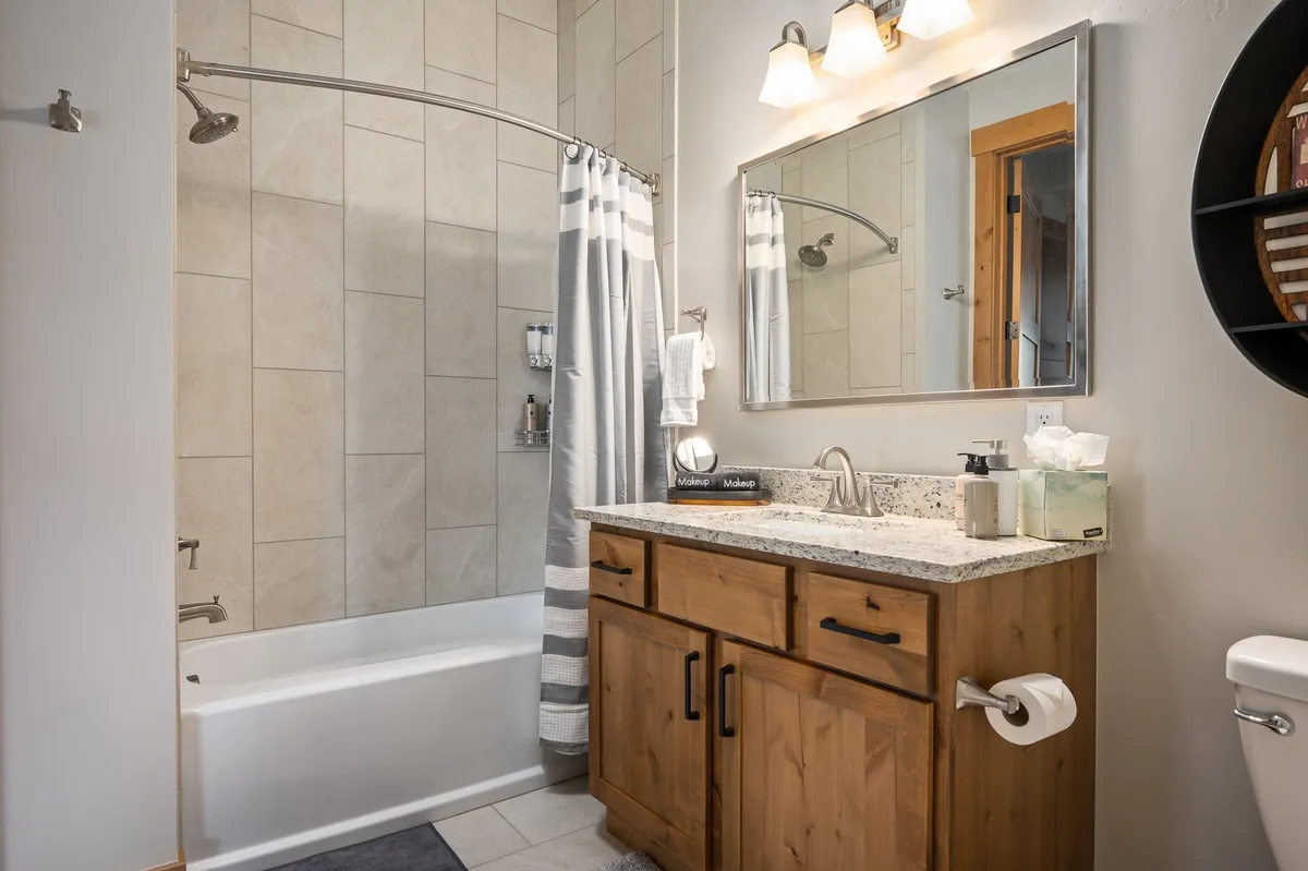 A contemporary bathroom featuring a large mirror, elegant vanity with sink, bathtub with shower curtain, and sleek fixtures. The space exudes a spa-like feel, emphasizing relaxation and self-care.