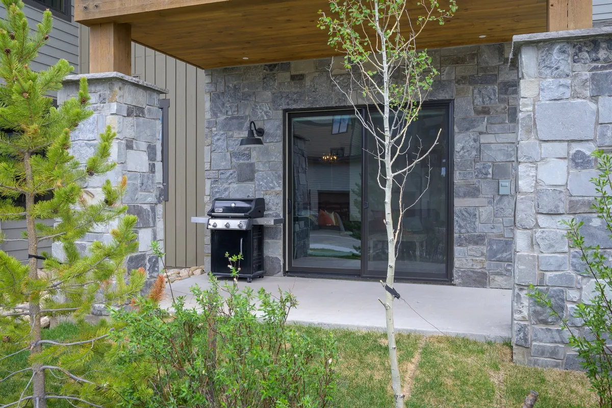 Outdoor grilling area next to a stone wall, with a sliding glass door leading inside and lush greenery surrounding the patio. The cozy ambiance suggests a welcoming spot for gatherings, sunset barbecues, and starlit evenings, echoing the versatility of the patio space.