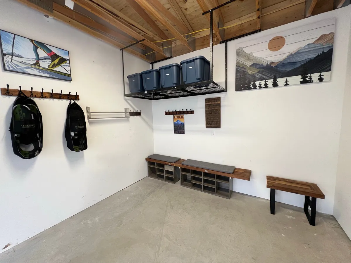 A practical and welcoming interior space with prominent artwork of a skier, ample storage bins, and wooden benches. The area is designed for storing outdoor gear and preparing for—or unwinding after—adventures. The scene evokes a sense of readiness for mountain activities and efficient organization.