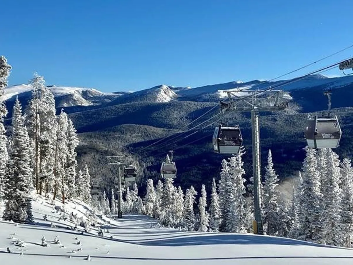 An exhilarating exterior shot of a gondola lift gliding above a snow-covered landscape with majestic mountain peaks in the distance. Skiers and snowboarders can be seen enjoying fresh powder, while the peaceful setting captures the beauty and adventure of alpine pursuits.