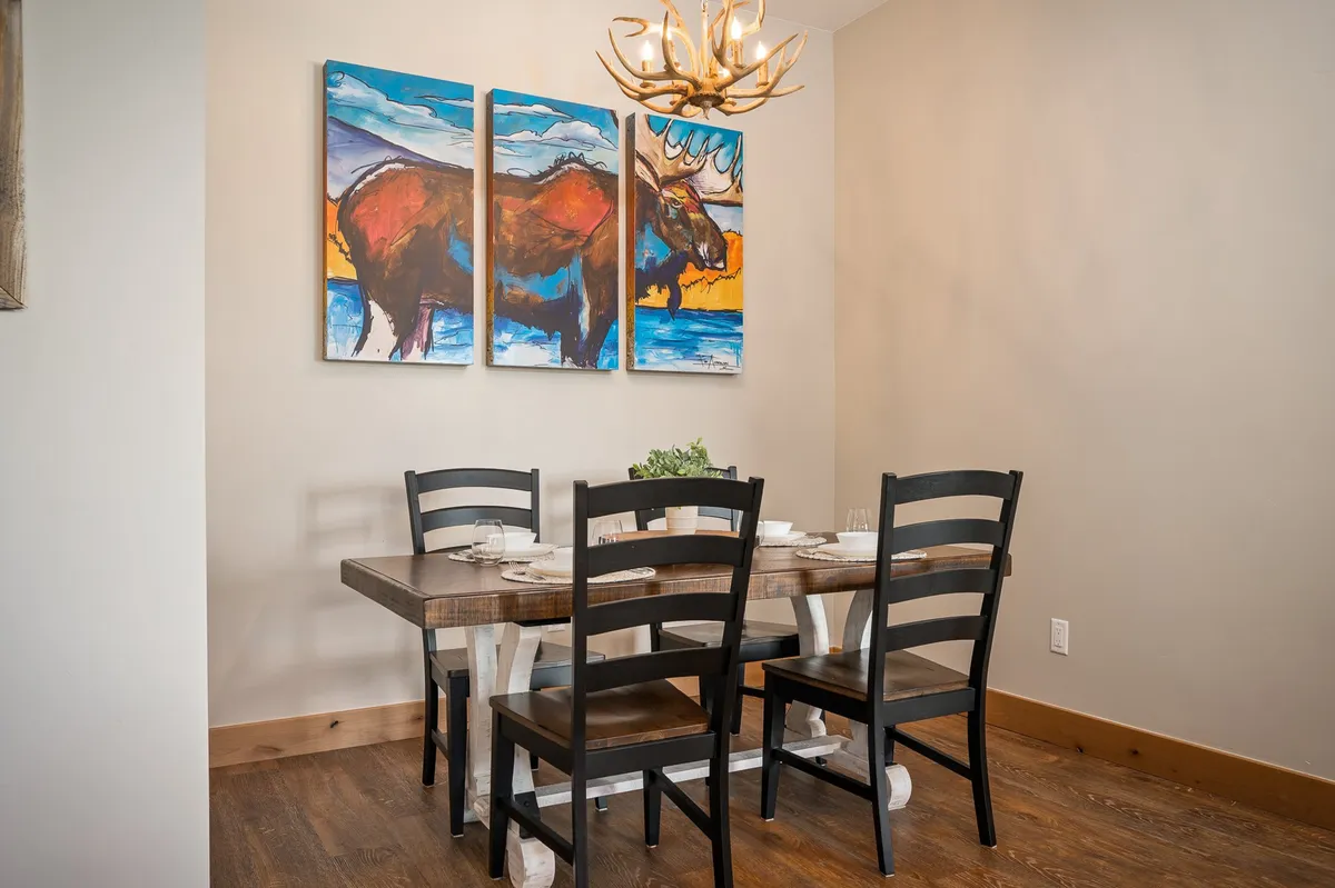 A dining area featuring a large table set beneath a chandelier, highlighted by tasteful wall art. The arrangement creates a mood that is both elegant and welcoming, ideal for family meals or celebrations.